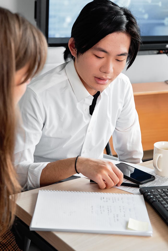 Asian man collaborating with a colleague in a modern office setting, focused on work.